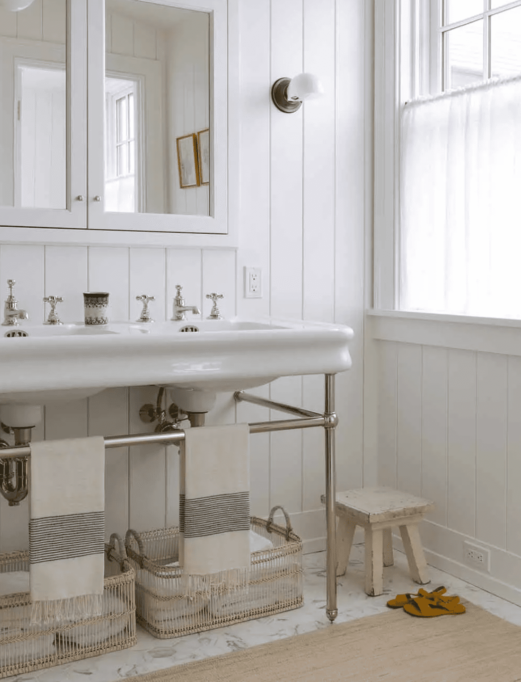 Une salle de bains blanche avec des sols en marbre blanc, des murs revêtus de bois blanc et une armoire à pharmacie blanche.