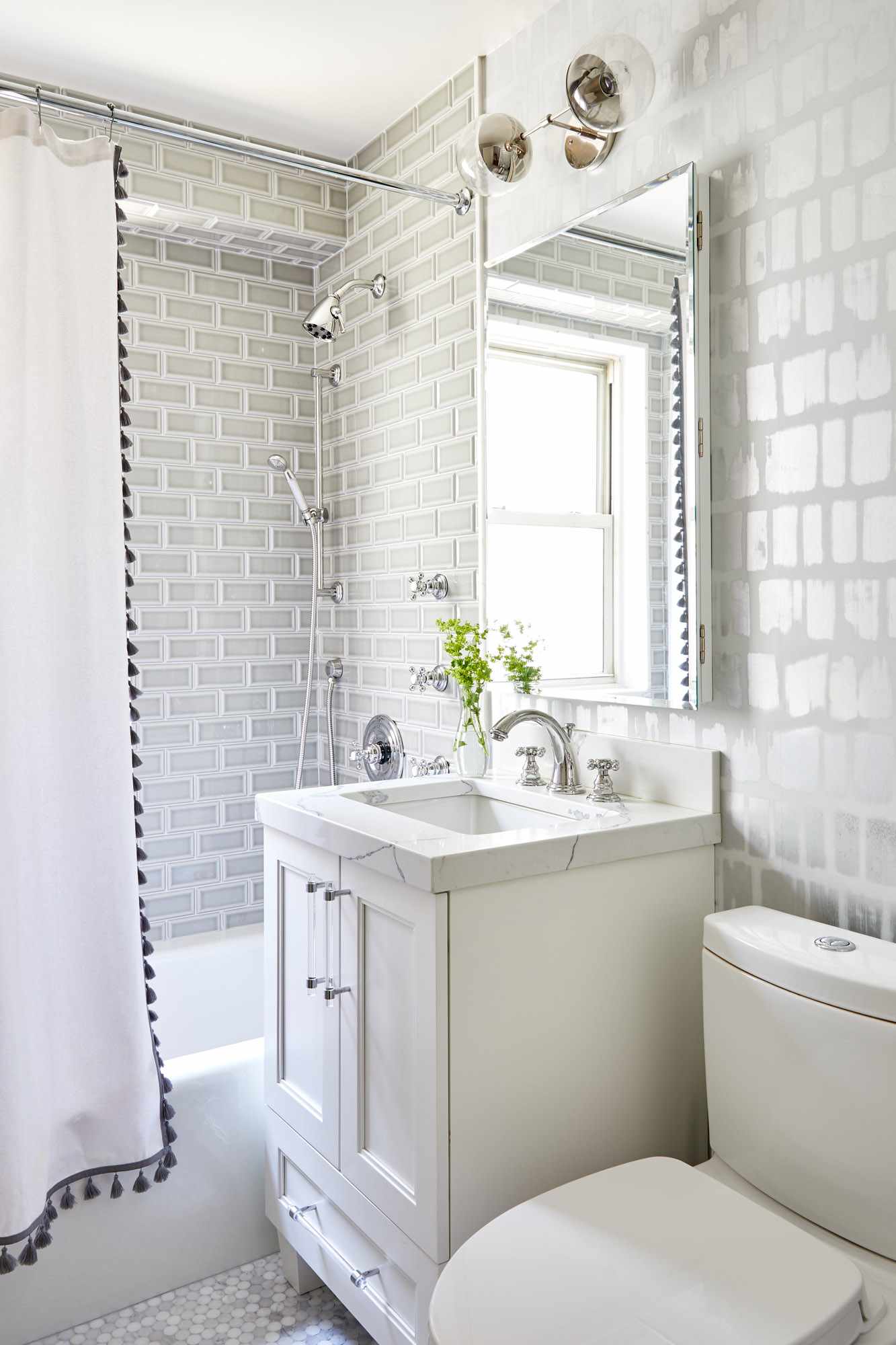 Salle de bains avec carrelage et papier peint gris et rideau de douche blanc avec pompons noirs