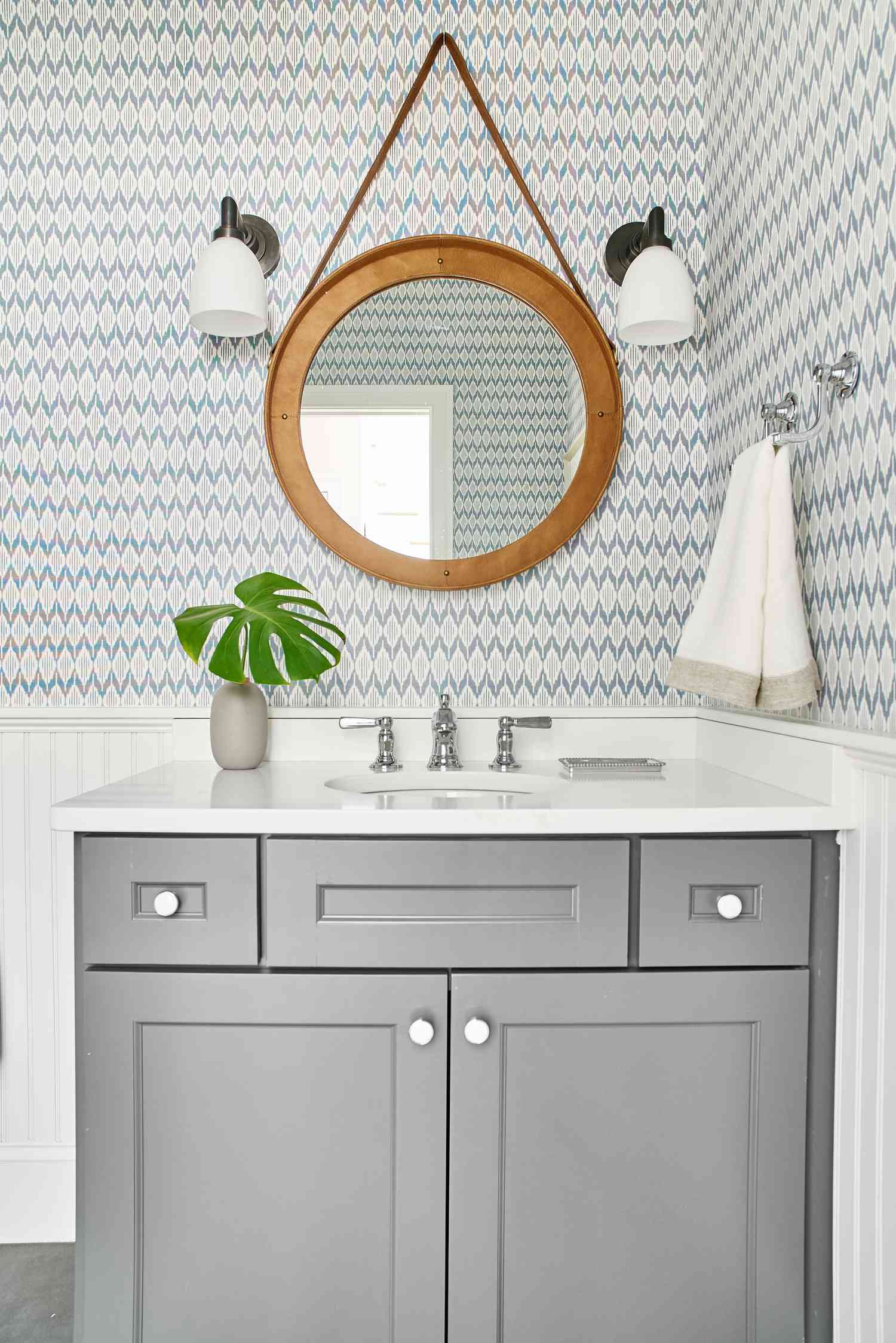 Meuble de toilette gris avec miroir rond en bois et papier peint bleu et blanc