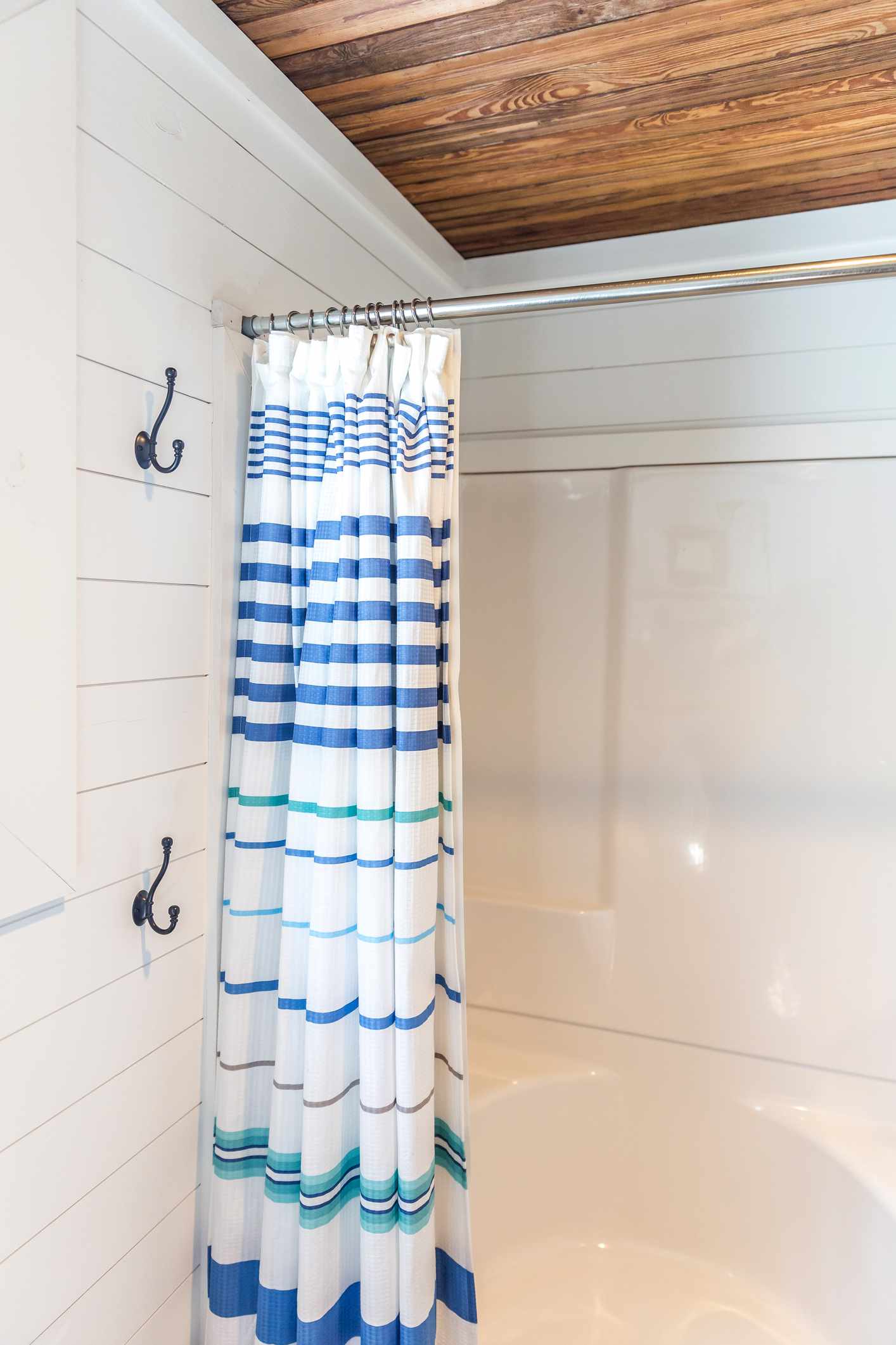 Salle de bains avec murs en shiplap blanc, plafond en bois teinté et rideau de douche à rayures.