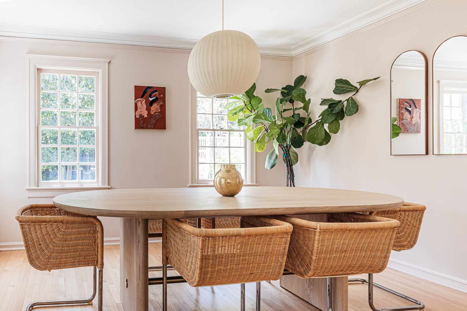 Salle à manger aux murs peints en beige neutre avec une table ovale et des chaises en osier au centre.