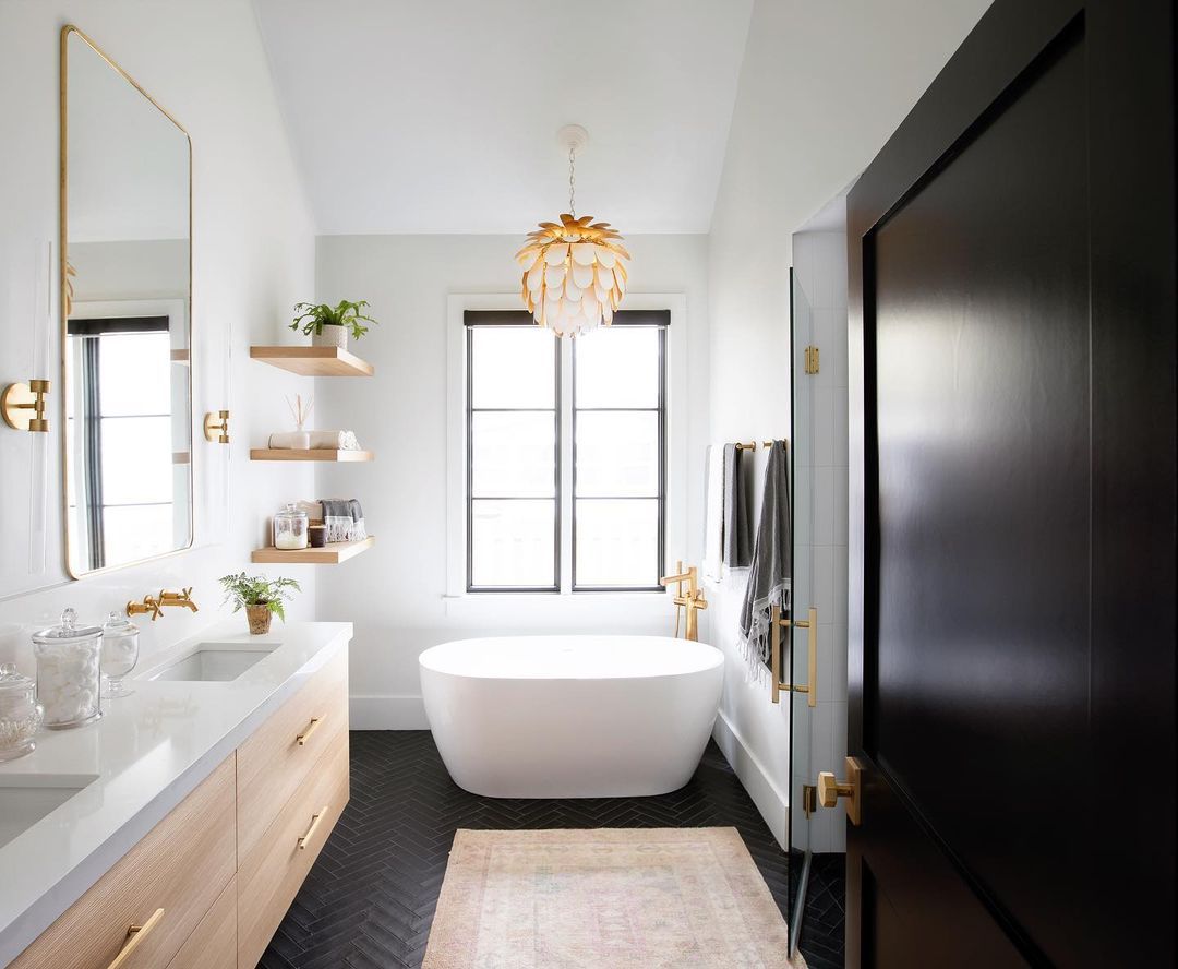 Une salle de bains avec des carreaux de sol noirs et un lustre doré au-dessus de la baignoire autoportante.