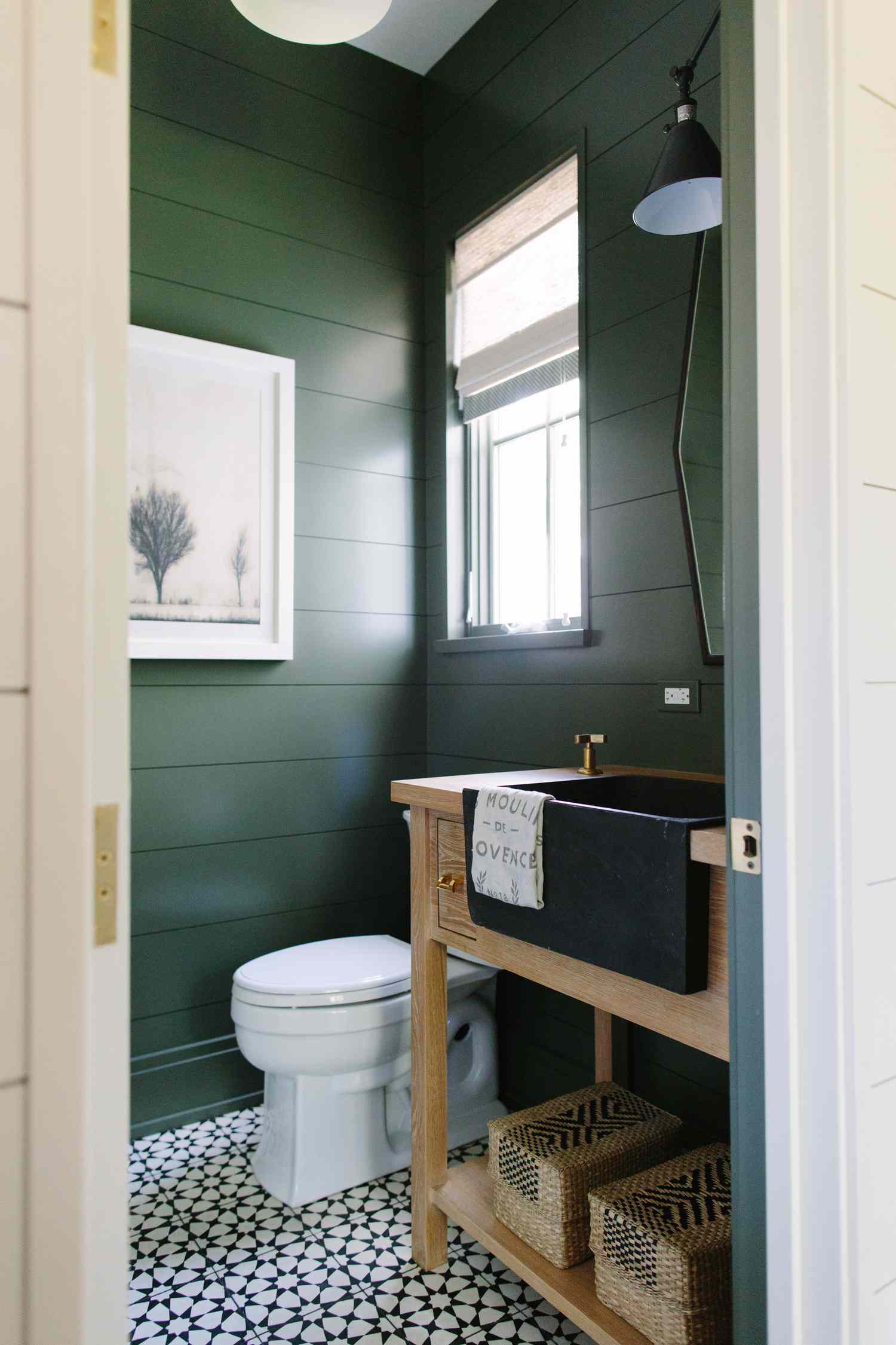 Une salle de bain vert foncé avec un évier de ferme noir et un meuble-lavabo en bois.
