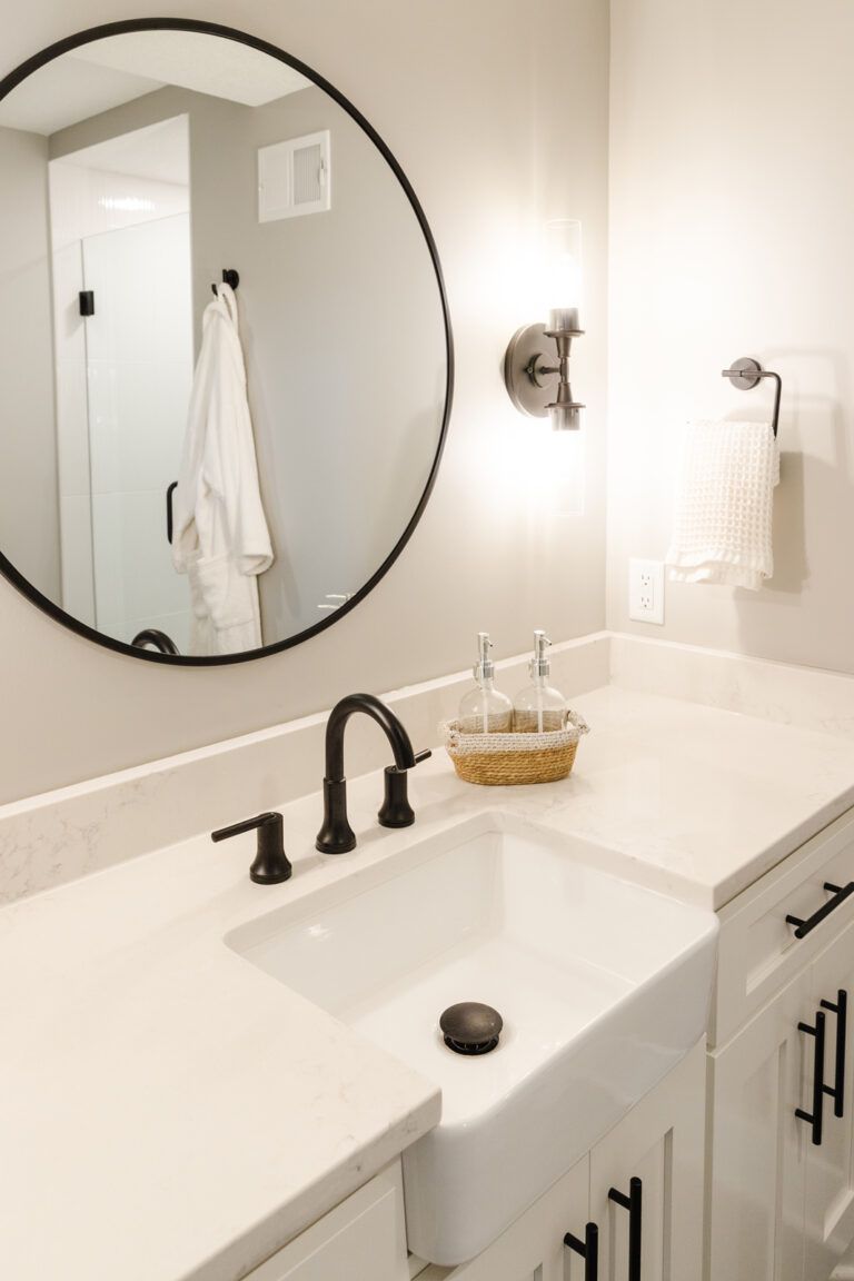 Une salle de bains avec un miroir rond et un comptoir blanc