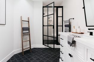 Salle de bain noire et blanche avec armoires blanches et porte de douche à rebord noir
