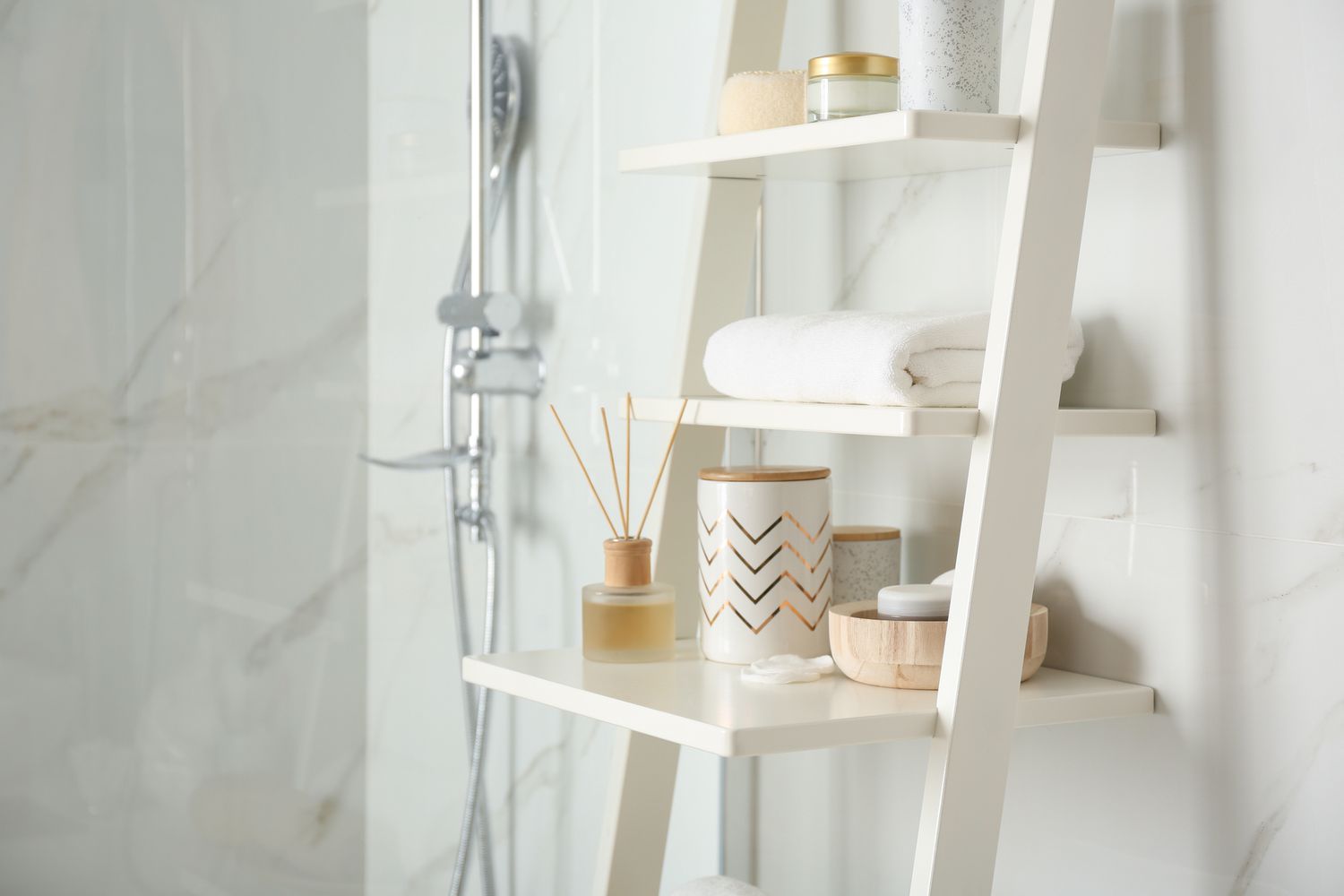 Etagère blanche en échelle remplie d'accessoires dans une salle de bain